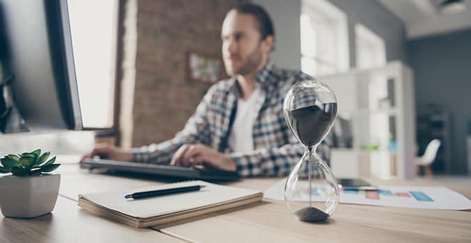 Man sitting at a computer with an hourglass trying to learn how to get better at Excel