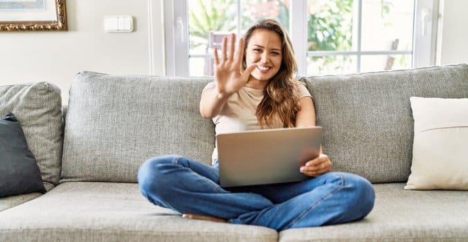 Woman sitting on couch with a laptop giving a high five sign after learning how to round to the nearest 5 in Excel